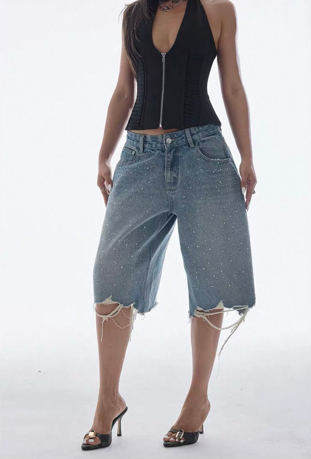 Person wearing a black sleeveless top and blue denim capri pants on a white background