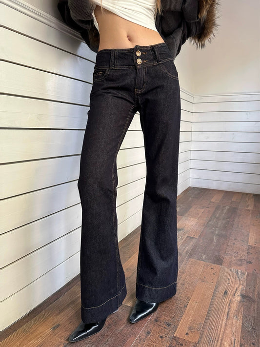 Person wearing black flared jeans against a white paneled wall.