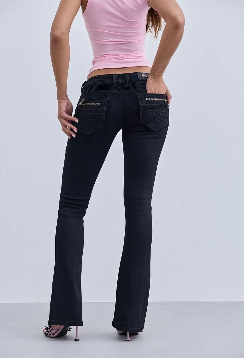 Person wearing black flared jeans and a pink top on a white background