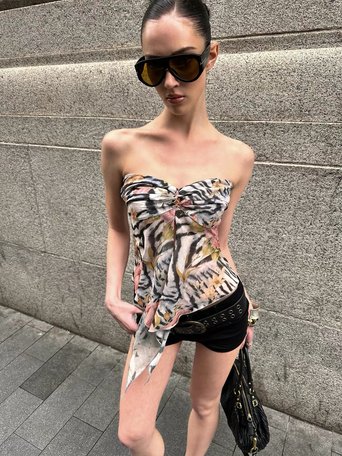 Woman wearing a strapless floral top and black shorts against a gray wall.