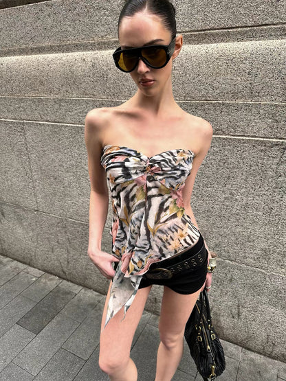 Woman wearing a strapless floral top and black shorts against a gray wall.