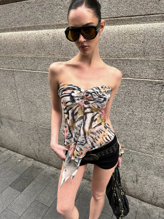 Woman wearing a strapless floral top and black shorts against a gray wall.
