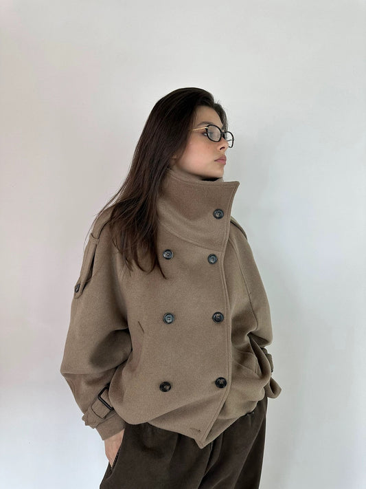 Person wearing a beige oversized jacket with black buttons on a plain background