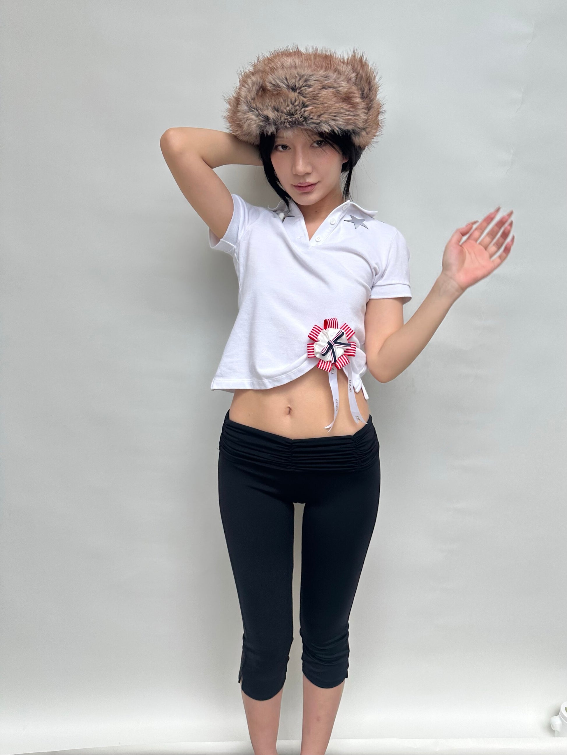 Person wearing a white top with a floral design and black pants, standing against a plain background.
