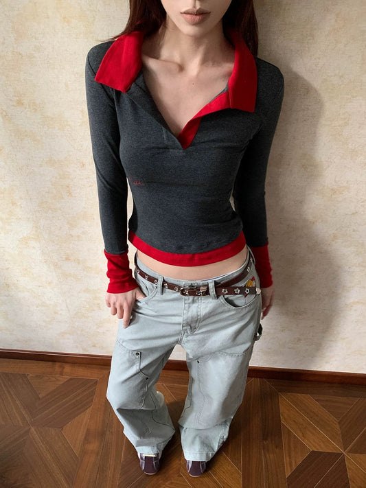 Person wearing a gray long-sleeve top with red accents and light blue jeans against a beige wall.