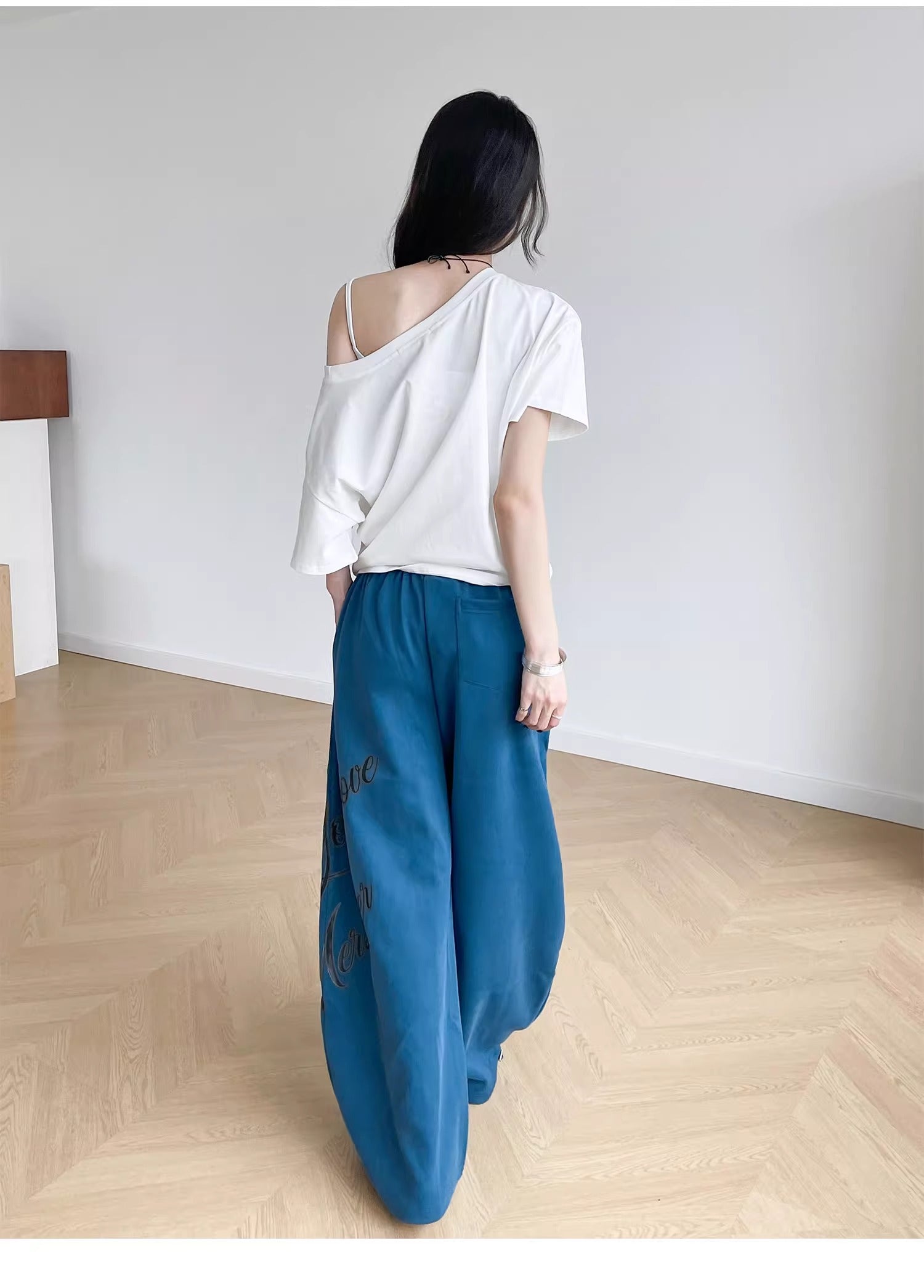 Person wearing a white top and blue pants standing in a minimalistic room with wooden flooring.