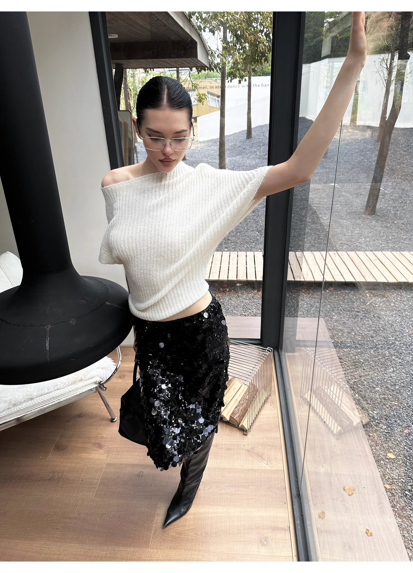 Woman in a white off-shoulder top and black sequin skirt standing indoors.