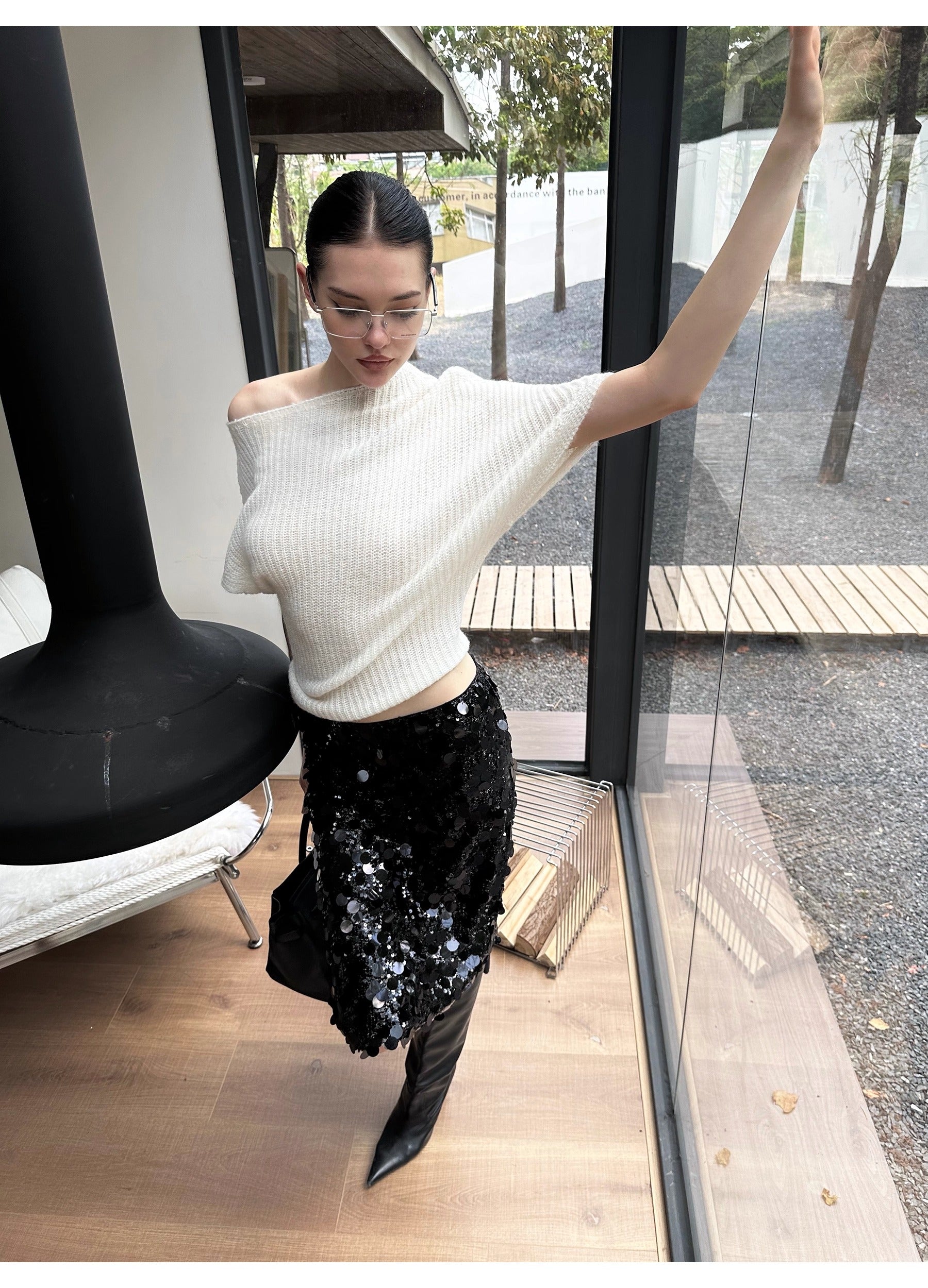 Woman in a white off-shoulder top and black sequin skirt standing indoors.