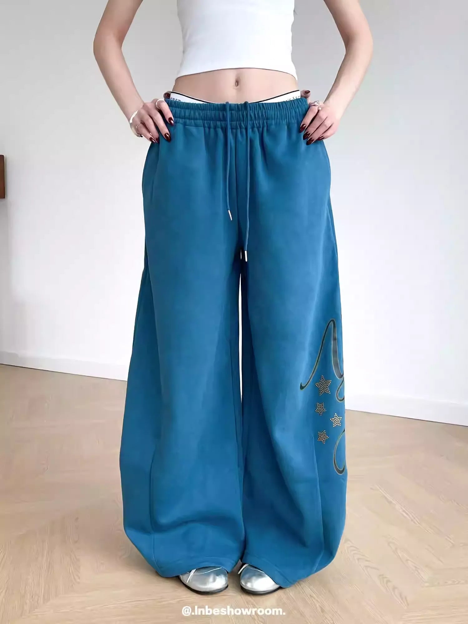 Person wearing blue wide-leg pants with a white top against a plain background